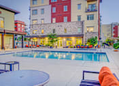 Thumbnail 8 of 24 - A swimming pool surrounded by a patio with chairs and a table.