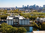 Thumbnail 25 of 27 - A large white building with a pool in the middle is surrounded by trees and water.