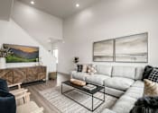 Thumbnail 21 of 26 - A living room with a grey sofa, a wooden cabinet, a glass coffee table and a painting on the wall.