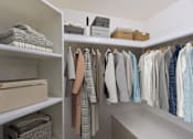 Thumbnail 50 of 51 - A white closet with clothes hanging and folded items on shelves.