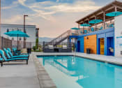 Thumbnail 14 of 34 - a swimming pool with blue chairs and umbrellas at a building with a pool
