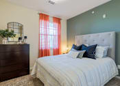 Thumbnail 9 of 26 - A bedroom with a large bed, a wooden dresser, and a window with orange curtains.