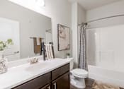 Thumbnail 8 of 26 - A white sink and toilet in a bathroom with a white tub and a grey shower curtain.