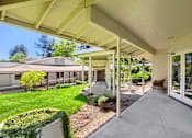 Thumbnail 12 of 15 - A covered walkway leads to a building with a brown chair on the right.