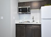Thumbnail 11 of 21 - A kitchen with a white refrigerator, a microwave, and a sink.