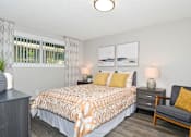 Thumbnail 8 of 21 - A bedroom with a patterned bedspread and a grey chair.
