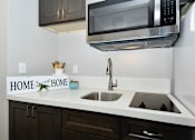 Thumbnail 12 of 21 - A kitchen with a white countertop and a black microwave above it.