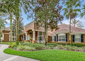 Thumbnail 4 of 19 - A house with a brown roof and tan walls is surrounded by greenery.