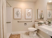 Thumbnail 5 of 15 - A bathroom with a toilet, sink, and two wall art pieces.