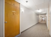 Thumbnail 14 of 31 - A long hallway with a wooden door on the left and carpeted flooring.