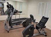 Thumbnail 4 of 25 - A gym with a treadmill, elliptical trainer and a stationary bike.