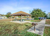 Thumbnail 5 of 14 - A pavilion with a wooden roof and a picnic table is surrounded by a grassy area.