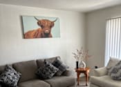 Thumbnail 8 of 27 - A living room with a grey couch and a cow picture on the wall.