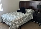 Thumbnail 10 of 27 - A bed with a patterned sheet and a black pillow is in a room with a wooden headboard.