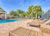 Thumbnail 13 of 15 - A poolside patio with a wicker chair and table.