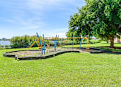 Thumbnail 6 of 15 - A playground with a swing set and a tree in the background.