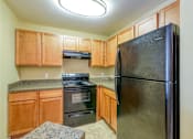 Thumbnail 4 of 15 - A kitchen with a black refrigerator, wooden cabinets, and a granite countertop.