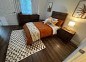 Thumbnail 7 of 14 - A bedroom with a bed, nightstand, and a painting of a palm tree on the wall.