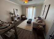 Thumbnail 2 of 14 - A living room with a grey couch, a wooden table, and a ceiling fan.