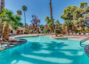 Thumbnail 12 of 32 - a swimming pool with palm trees and a building in the background at Pacific Harbors Sunrise Apartments, Las Vegas, NV, 89142