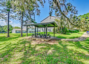 Thumbnail 3 of 25 - A picnic table is situated under a pavilion in a grassy area.