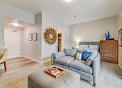 Thumbnail 18 of 28 - A living room with a grey couch and a wooden dresser.