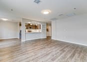 Thumbnail 6 of 28 - A spacious room with wooden flooring and a kitchen area in the background.