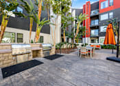 Thumbnail 40 of 42 - A patio with a grill and chairs is surrounded by trees.
