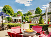 Thumbnail 2 of 28 - a patio with red chairs and tables and a fire pit at Residences at Stevens Pond, Massachusetts, 01906