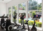 Thumbnail 11 of 28 - a gym with exercise equipment and windows overlooking a pool at Residences at Stevens Pond, Massachusetts