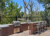 Thumbnail 26 of 32 - a brick outdoor kitchen with two bbqs and a table with chairs at Arcadia Apartments, Centennial