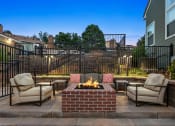 Thumbnail 27 of 32 - a brick patio with a fireplace and chairs at Apartments at Arcadia Apartments, Centennial, CO