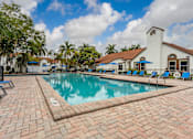 Thumbnail 10 of 19 - A pool with a brick walkway and a white building in the background.
