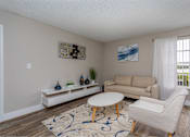 Thumbnail 2 of 19 - A living room with a white couch, a white coffee table, and a white chair.