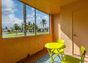 Thumbnail 8 of 19 - A yellow table and chairs are in front of a window with a view of a palm tree and a blue sky.