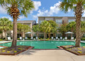Thumbnail 23 of 30 - a swimming pool with palm trees and a building in the background at Summerwind, Pearland, TX 77584