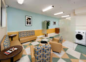 Thumbnail 18 of 21 - A laundry room with a washer and dryer, a table, and chairs at Skye at Belltown Apartments, Washington 98121