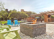 Thumbnail 11 of 21 - A fire pit is in the middle of a gravel area with blue and green chairs around it at Skye at Belltown Apartments, Seattle, WA 98121