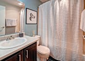 Thumbnail 25 of 25 - A bathroom with a white sink, toilet, and a shower curtain at Brackett Apartments, Edmonds, WA, 98020