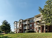 Thumbnail 32 of 38 - Three story brick apartment building on grassy hillside at Wyndchase Aspen Grove Apartments, Franklin