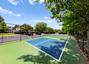 Thumbnail 10 of 33 - A tennis court surrounded by a fence and trees.