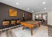 Thumbnail 17 of 33 - A pool table is surrounded by four chairs in a room with a brown wall and a painting.