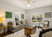 Thumbnail 25 of 33 - A living room with a grey couch, a wooden coffee table, and a ceiling fan.