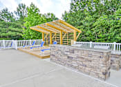 Thumbnail 8 of 17 - A wooden pavilion with a stone wall and two chairs.