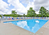 Thumbnail 12 of 17 - A large outdoor swimming pool surrounded by trees and a fence.