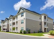 Thumbnail 9 of 14 - A large apartment building with a parking lot in front.
