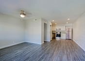 Thumbnail 2 of 15 - A kitchen with white cabinets and a refrigerator is visible through an open door in a room with wooden floors.