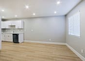 Thumbnail 2 of 13 - an empty living room with a kitchen with white cabinets and a window