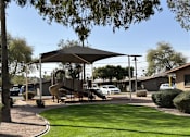 Thumbnail 1 of 4 - A playground with a slide and a canopy is surrounded by a grassy area and a sidewalk.