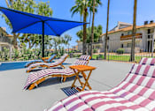 Thumbnail 11 of 28 - Pool patio area with red and white stripped lounge chairs and a table with umbrellas at Tides on McDowell, Phoenix, AZ